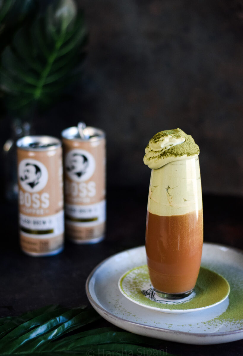 An elegantly styled Matcha in a tulip glass, sprinkled with green matcha with opened cans of BOSS Coffee in the background