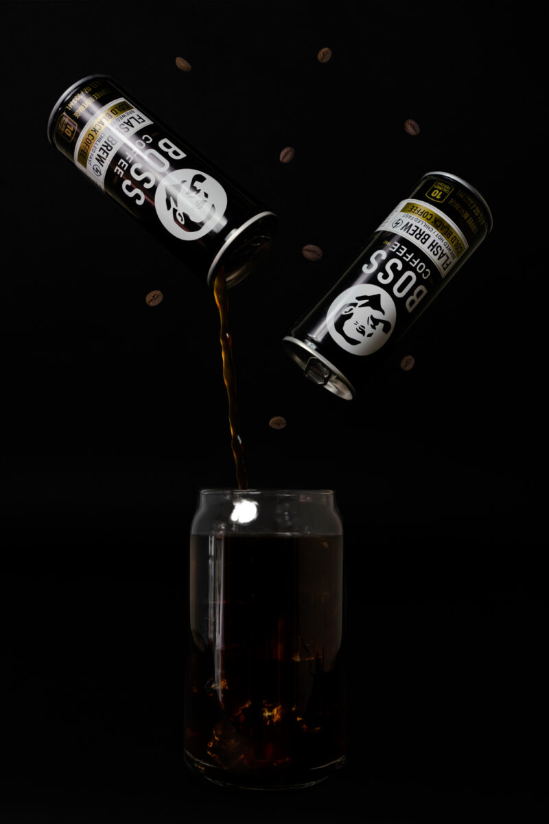 Two floating BOSS Coffee cans being poured into a glass on a black background.