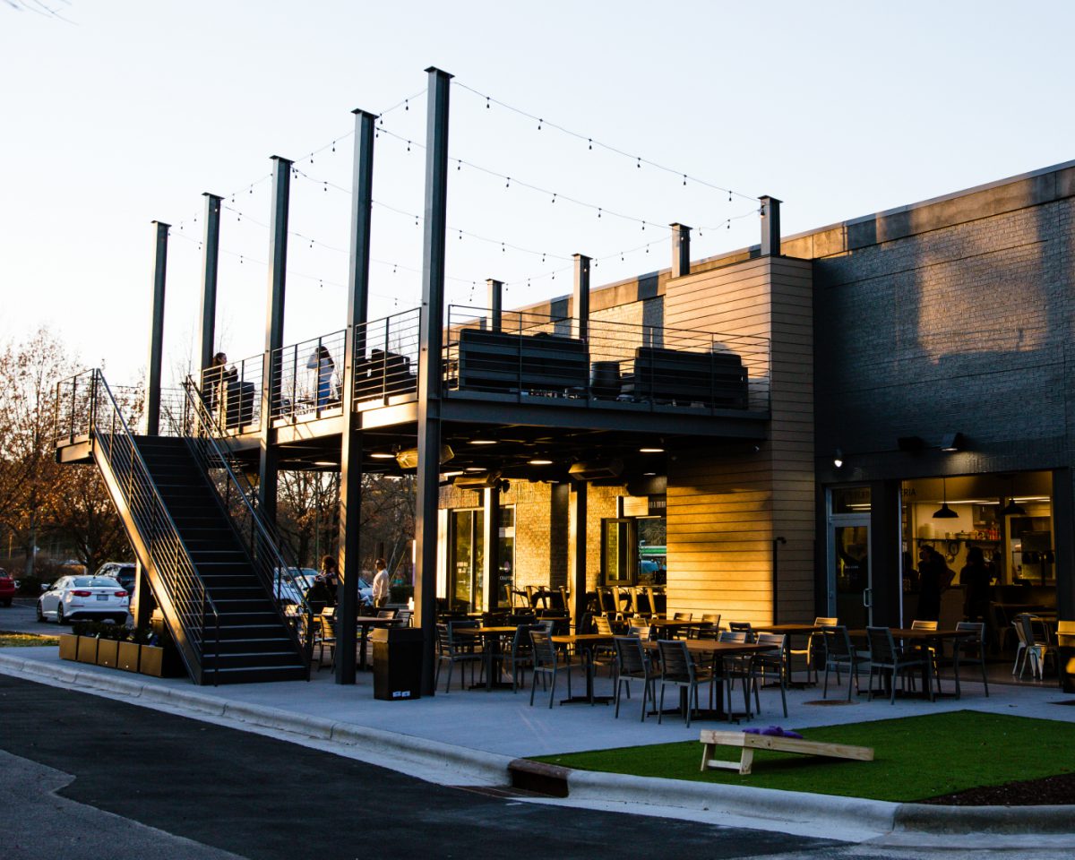 An exterior photo of Craften Food Hall in Knightdale, North Carolina as the sun sets on the outdoor dining area, rooftop patio, and cornhole boards.