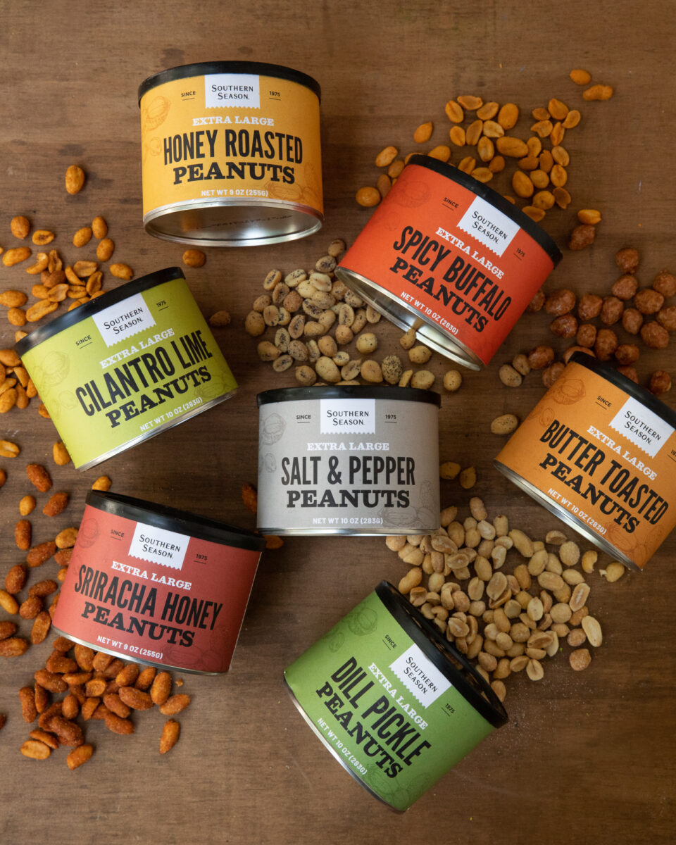 An assortment of Southern Season's Peanut flavors, poured onto a wooden background with the colorful tins
