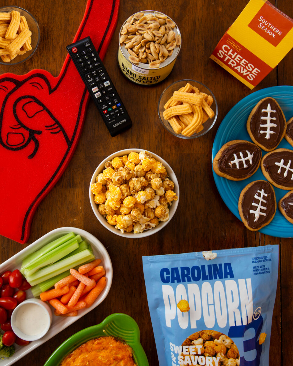 A top down photo of Southern Season's best snacks for the Superbowl, including their Carolina Popcorn Co Trio Mix and Cheese Straws.