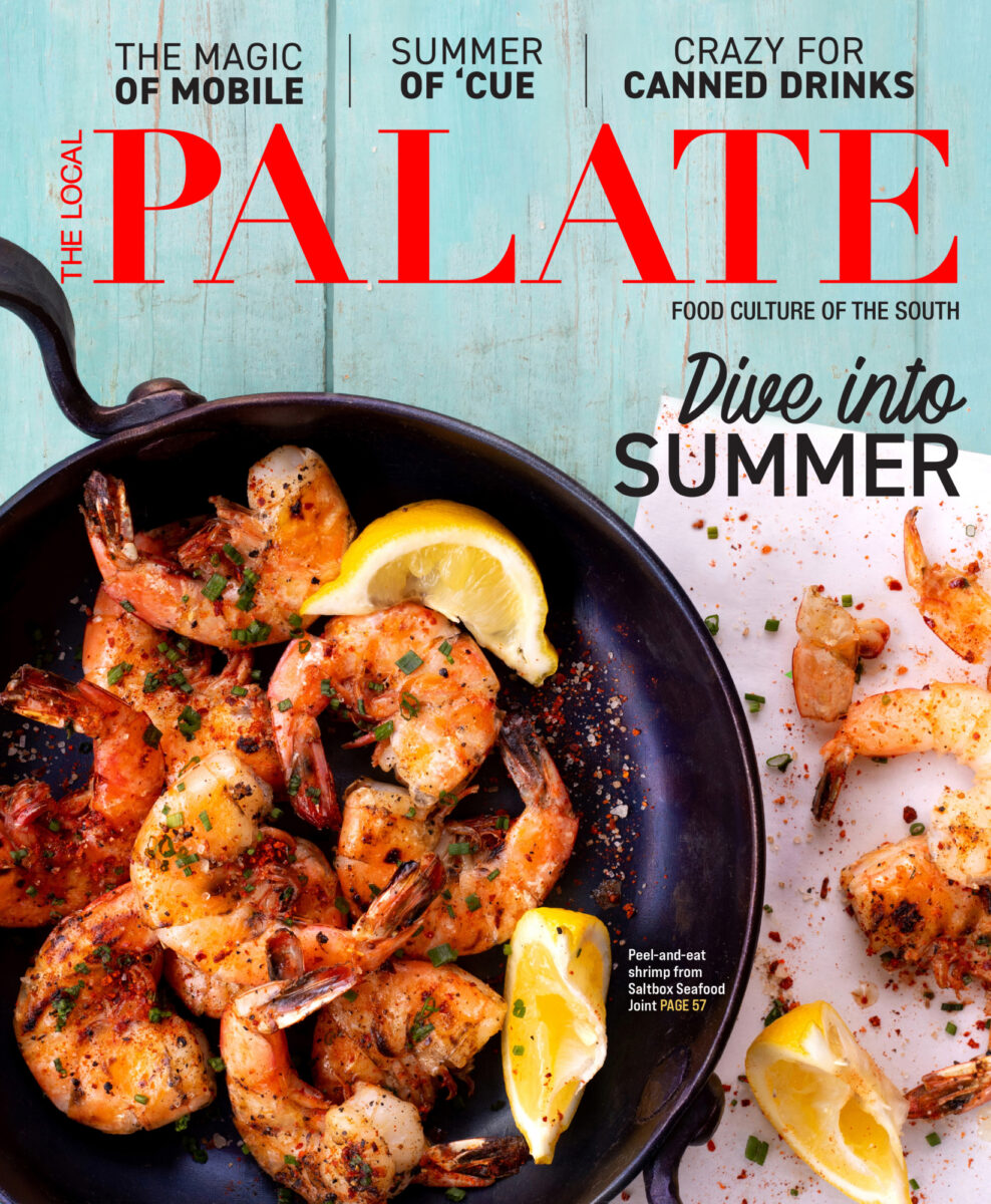 A top down photo of the June 2021 cover for The Local Palate by Food Seen with a cast iron skillet filled with grilled shrimp on a light blue picnic table.
