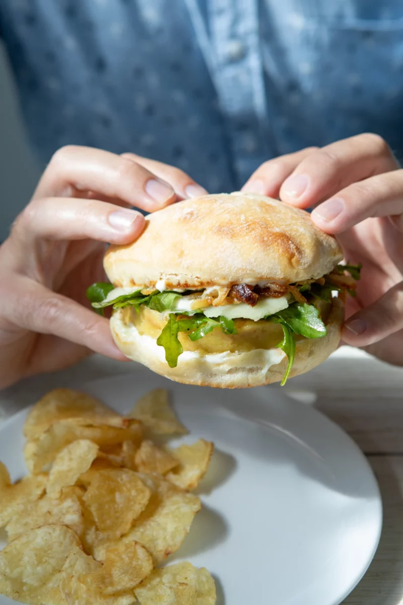 A person holding a Mr Burgy and Co burger over a plate of chips