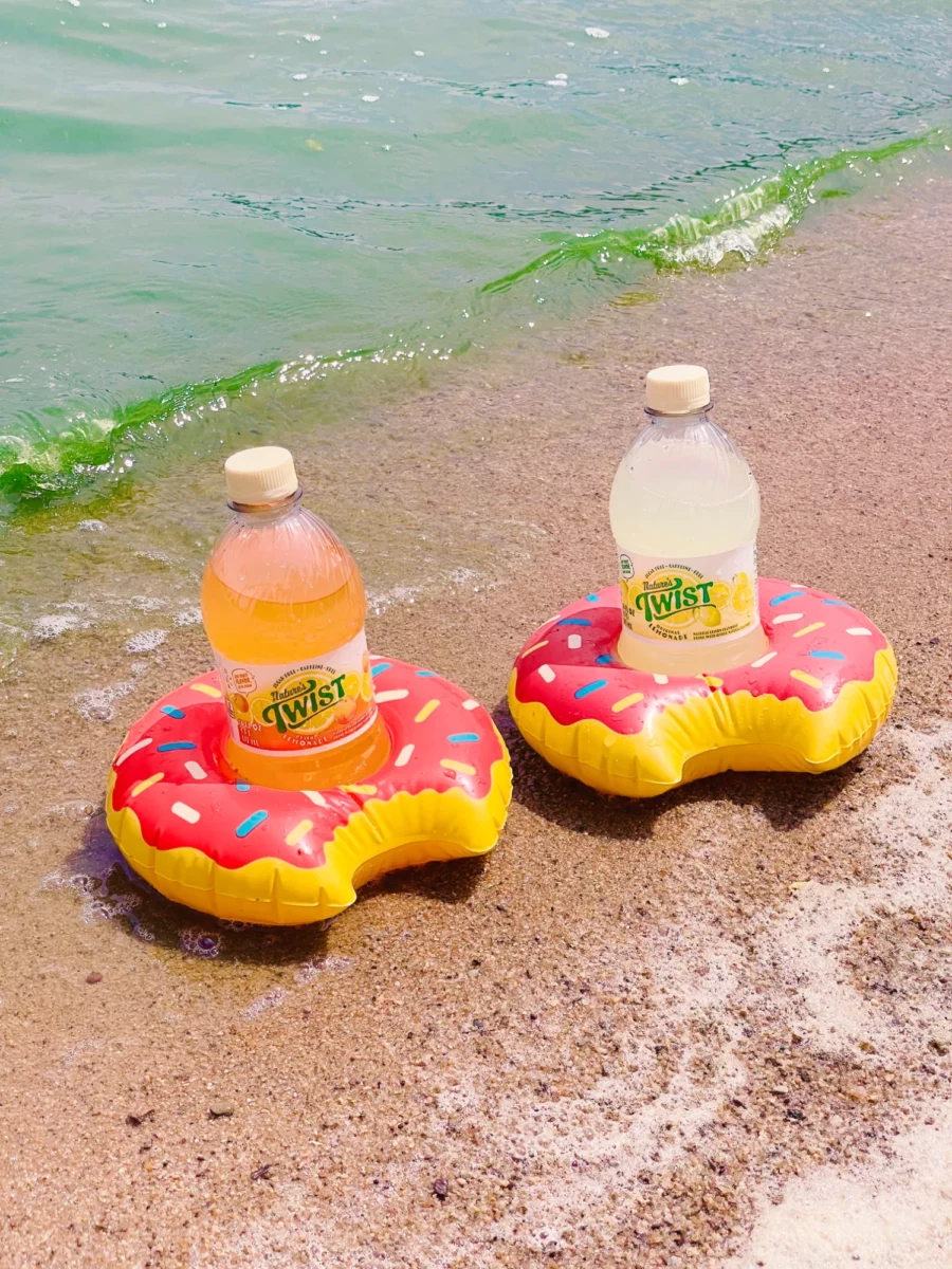 Two bottles of Nature's Twist in mini pool floats, sitting on the beach with waves from the lake crashing in behind them