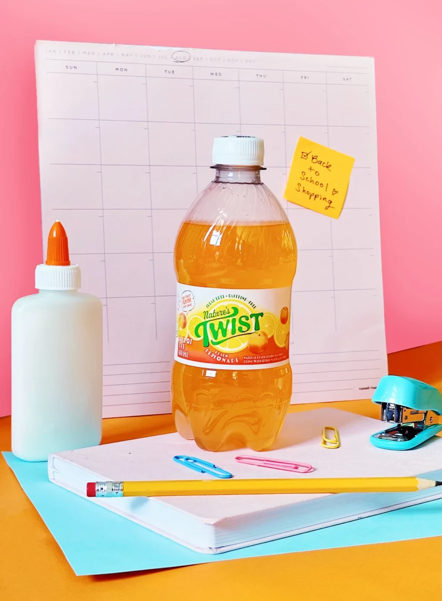 A bottle of Nature's Twist Peach Lemonade sitting on top on a notebook and surrounded by other school supplies