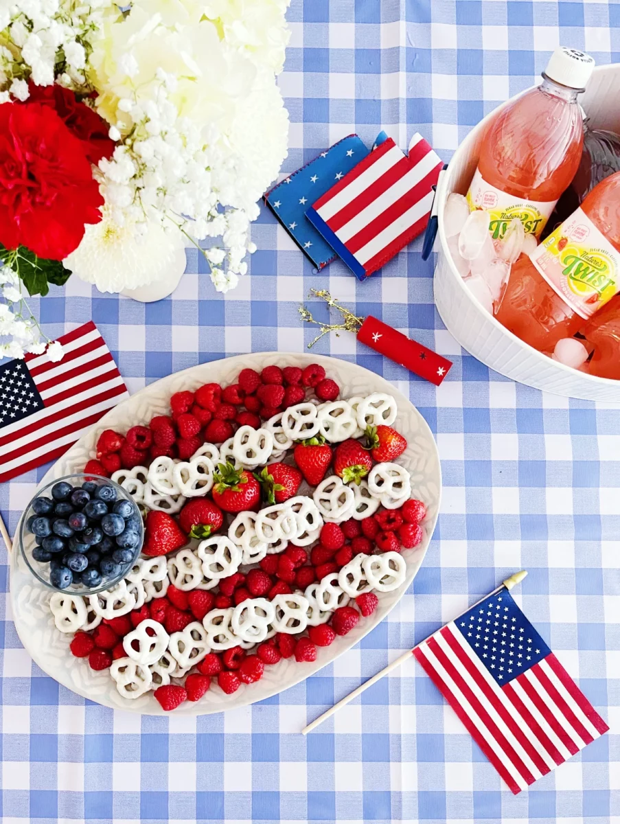 A Fourth of July snack spread with raspberries, yogurt covered pretzels and blueberries making an American flag with Nature's Twist strawberry lemonade sitting in a bucket of ice.